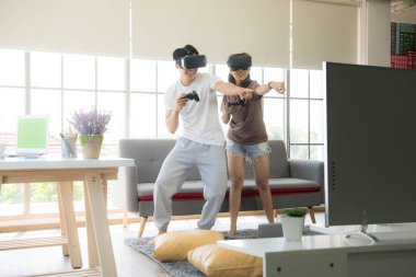 Genç mutlu Asyalı çift dairelerinde sanal gerçeklik gözlüğü takıp video oyunu oynuyorlar.