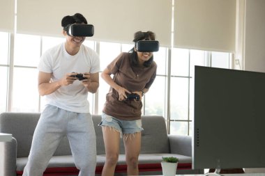 Genç mutlu Asyalı çift dairelerinde sanal gerçeklik gözlüğü takıp video oyunu oynuyorlar.