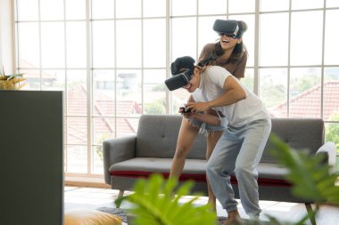 Genç mutlu Asyalı çift dairelerinde sanal gerçeklik gözlüğü takıp video oyunu oynuyorlar.