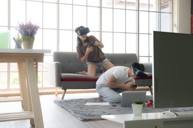 Genç mutlu Asyalı çift dairelerinde sanal gerçeklik gözlüğü takıp video oyunu oynuyorlar.