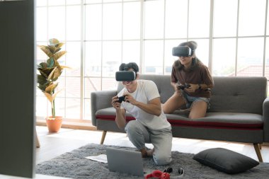 Genç mutlu Asyalı çift dairelerinde sanal gerçeklik gözlüğü takıp video oyunu oynuyorlar.