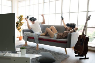 Genç mutlu Asyalı çift dairelerinde sanal gerçeklik gözlüğü takıp video oyunu oynuyorlar.