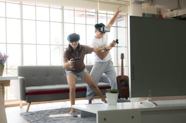 Genç mutlu Asyalı çift dairelerinde sanal gerçeklik gözlüğü takıp video oyunu oynuyorlar.