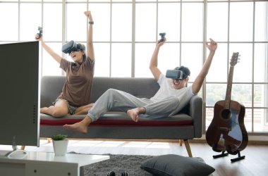 Genç mutlu Asyalı çift dairelerinde sanal gerçeklik gözlüğü takıp video oyunu oynuyorlar.