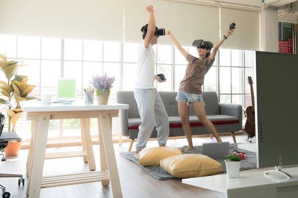 Genç mutlu Asyalı çift dairelerinde sanal gerçeklik gözlüğü takıp video oyunu oynuyorlar.