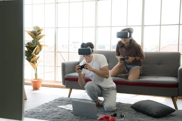Genç mutlu Asyalı çift dairelerinde sanal gerçeklik gözlüğü takıp video oyunu oynuyorlar.