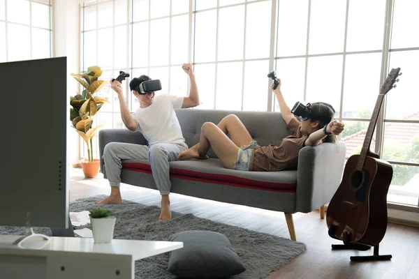 Genç mutlu Asyalı çift dairelerinde sanal gerçeklik gözlüğü takıp video oyunu oynuyorlar.