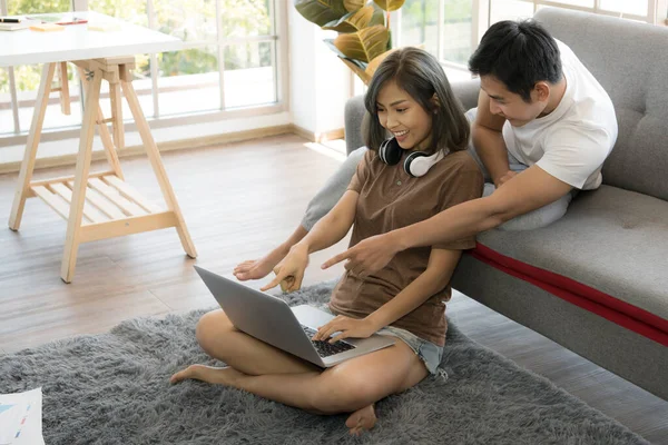 Mutlu Asyalı çift evde dizüstü bilgisayarla online alışveriş yapıyor.