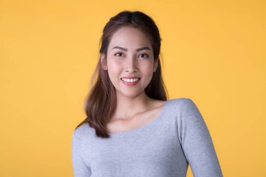 Sarı arka planda izole edilmiş genç Asyalı mutlu kadının portresi.