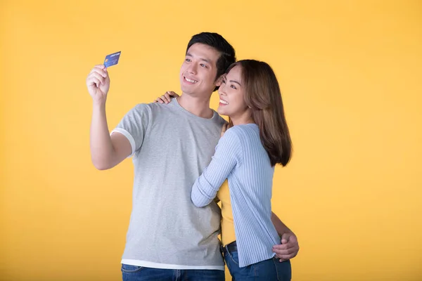 Young Asian couple with credit card isolated on yellow background