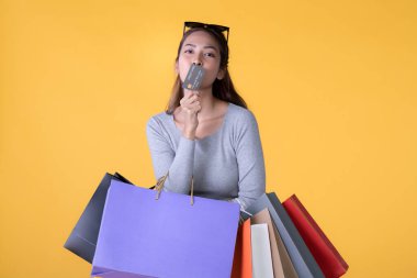 Sarı arka planda renkli alışveriş torbaları ve kredi kartıyla güzel bir Asyalı kadın.