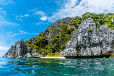 Parlak mavi gökyüzünün altında kayalık uçurumlar ve berrak turkuaz suların yer aldığı çarpıcı kıyı manzarası.