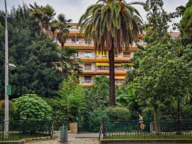 Kadın çitin kapısını açar ve bir pikniğin kapalı yeşil bahçesine girer