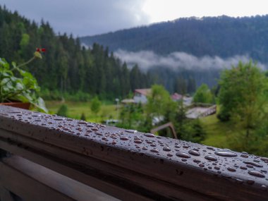 Açık balkon kapısından alçak bulutların, vahşi ormanın, Carpathian Trostyan dağının, sandalye kaldırma koltuklarının ve istasyon binasının üzerinden bak. Tahta korkuluklara düşen yağmur damlalarıyla ıslak balkon..