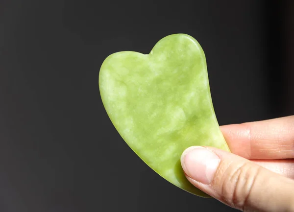 Elinde yeşil Jade doğal değerli Gua sha aracı. Kendi kendine masaj aracı