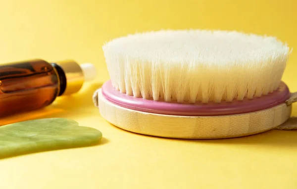 Dry body brush, oil bottle and gua sha massager at yellow background. Beauty treatment concept