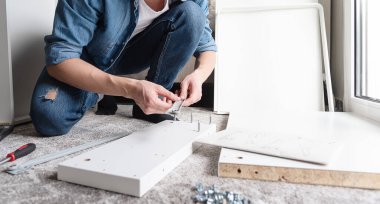 Konsantre genç adam ev için yeni mobilya montajı için araçlar seçiyor 