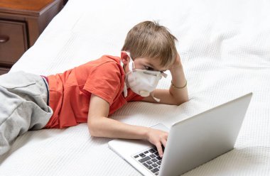 Laptop kullanan tıbbi maskeli bir çocuk. Covid-19 karantina, online okul konsepti