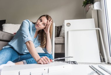 Yorgun bir kadın evde mobilya monte ediyor.