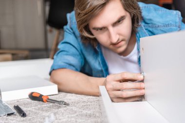Konsantre genç adam ev için yeni mobilyalar monte ediyor.