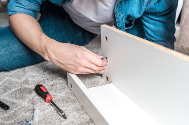 Yoğunlaşmış genç adam ev için yeni mobilyalar topluyor yerde yatıyor.