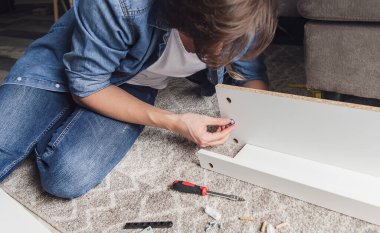 Yoğunlaşmış genç adam ev için yeni mobilyalar topluyor yerde yatıyor.