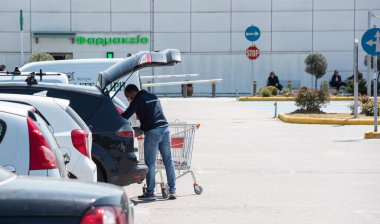 Selanik, Yunanistan - 11 Nisan 2020: Süpermarketin otoparkındaki bagaja alışveriş poşetleri koyan adam.