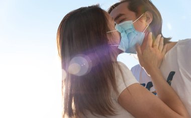 Genç bir adam ve kadın cerrahi maske takarak öpüşüyor, karantina altında, Covid-19 koruması altında. Koronavirüs salgını sırasında aşk.