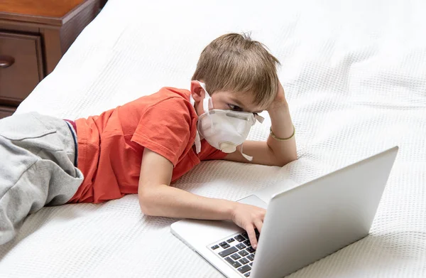 Laptop kullanan tıbbi maskeli bir çocuk. Covid-19 karantina, online okul konsepti