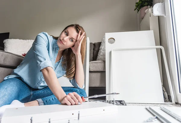 Yorgun bir kadın evde mobilya monte ediyor.