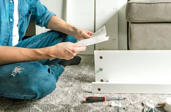 Man reading the instructions to assemble furniture at home in the living room