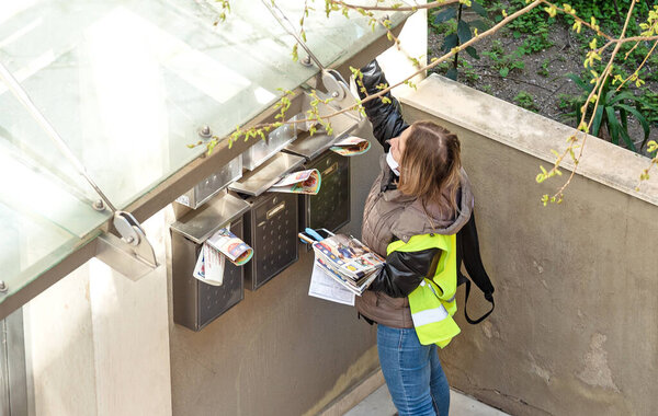 Thessaloniki, Greece - April 9, 2020: Woman with protective face mask working outdoors distributing advertising leaflets to post boxes. Working during quarantine of Covid-19.