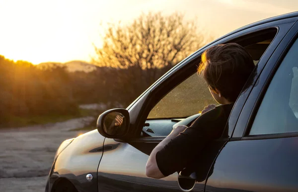 Young man sitting in car and looking at nature during sunset. Local trip concept.