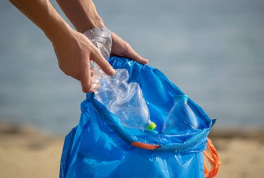 Mavi çöp torbasında plastik şişeleri toplayan el. Kumsalda temizlik yapmak.. 
