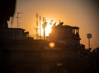 Şehir çatılarının üzerinde baca ve antenlerle gün batımı