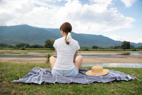 Young woman sitting at ease by the lake in silence with mountain at background