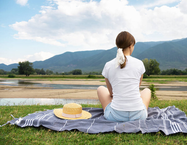 Young woman sitting at ease by the lake in silence. Social distancing holidays