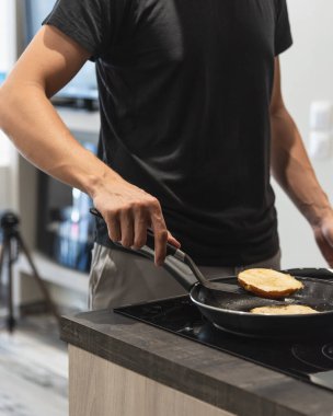 Genç adam tavada hamburger ekmeği kızartıyor.