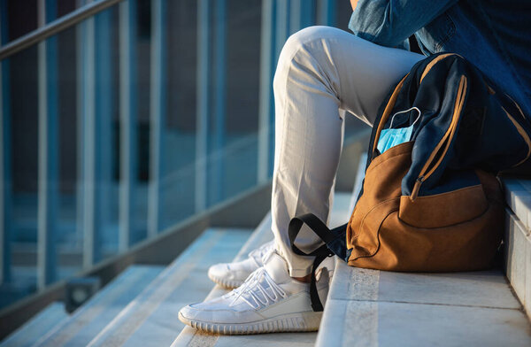 Man with backpack and face mask sitting on stairs at university campus.