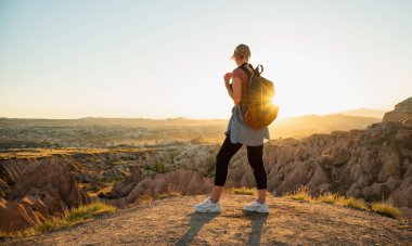 Sırt çantalı genç bir gezgin vadide gün batımına bakan güzel manzaraya bakıyor.