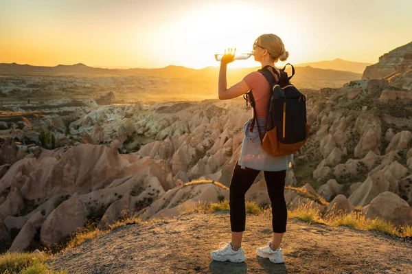 日没時に渓谷の息をのむような景色を持つ山の頂上に水を飲む女性バックパッカー — ストック写真