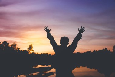 Günbatımında mutlu bir şekilde kaldırdı kollarını açarak duran genç bir adam silüeti.