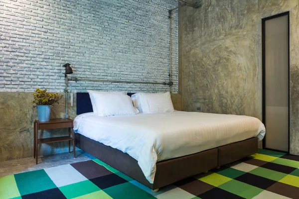 Bedroom with concrete wall and brick wall,carpet, bed, lamp and vase of dried flowers