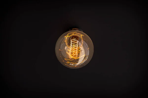 Old-fashioned light bulb turned on. On the dark surface, the concept of creativity in decorative design.