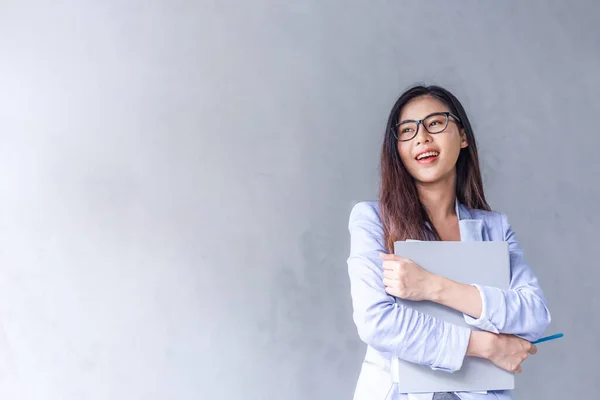 Beautiful business woman wears glasses to be a happy Asian smile In the mobile, the file is in the office On a gray background