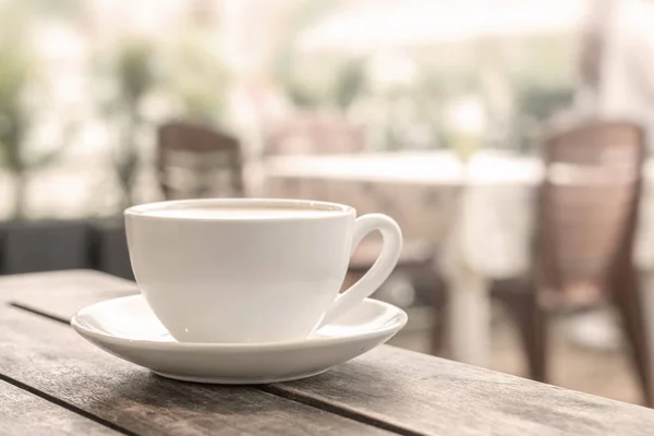 a white coffee mug stands on a wooden table in an outdoor coffee shop. light blurred background. close up.