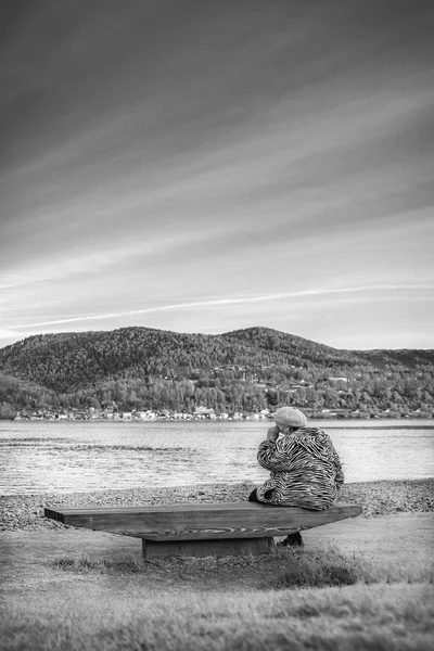 the old grandmother is sad and crying on the Bank of a beautiful river. black and white dramatic photo. veertical viev.