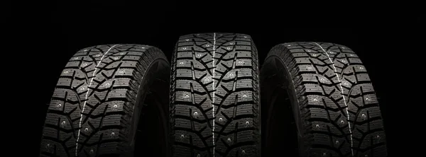 three studded winter tires wheels in a row on a black background, panoramic shot.