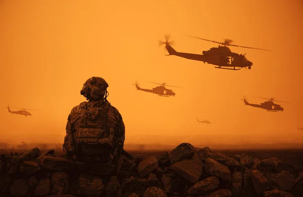Military helicopter and forces in desert and one soldier sits and looks at the battle field