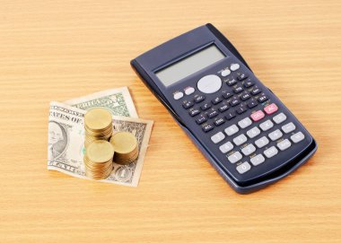 Hesap makinesi ve dolar paraları ahşap masaya istiflenmiş.